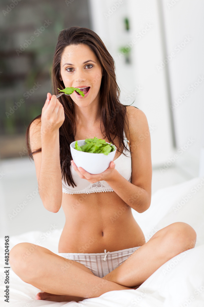 healthy young woman eating green salad on bed healthy young woman eating green salad on bed