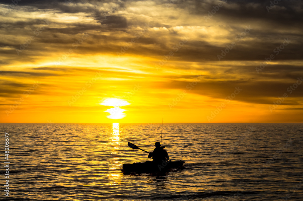 Fisherman in the kayak on the ocean in front of dramatic sunset