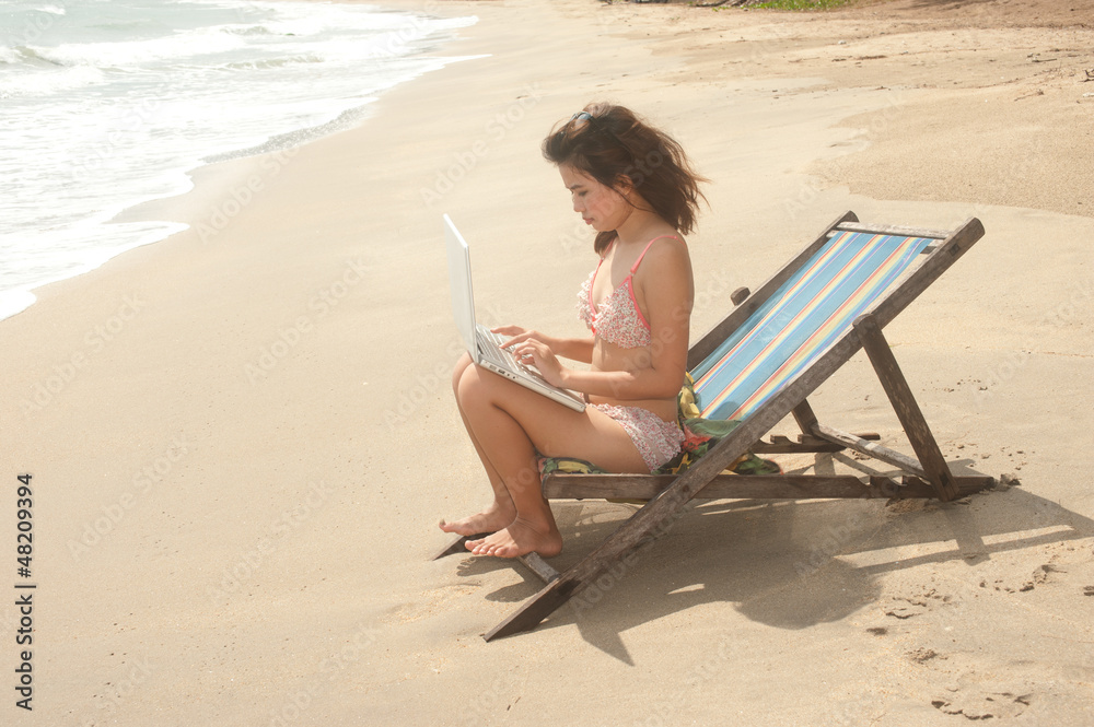 Pretty Asian woman working with laptop on beach bed .