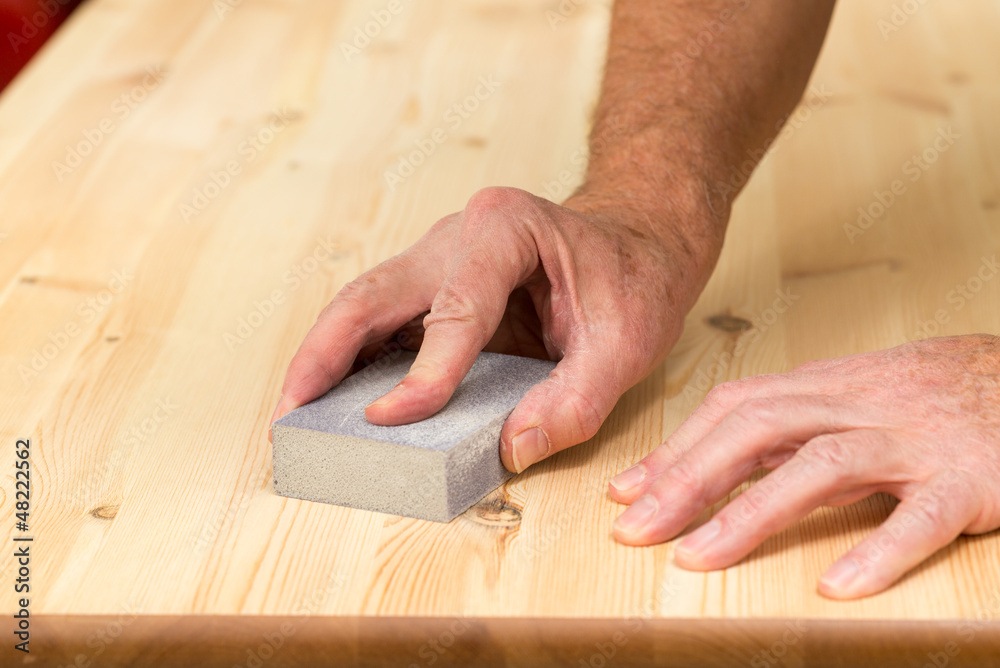 Mans hand on sanding block on pine wood Mans hand on sanding block on pine wood