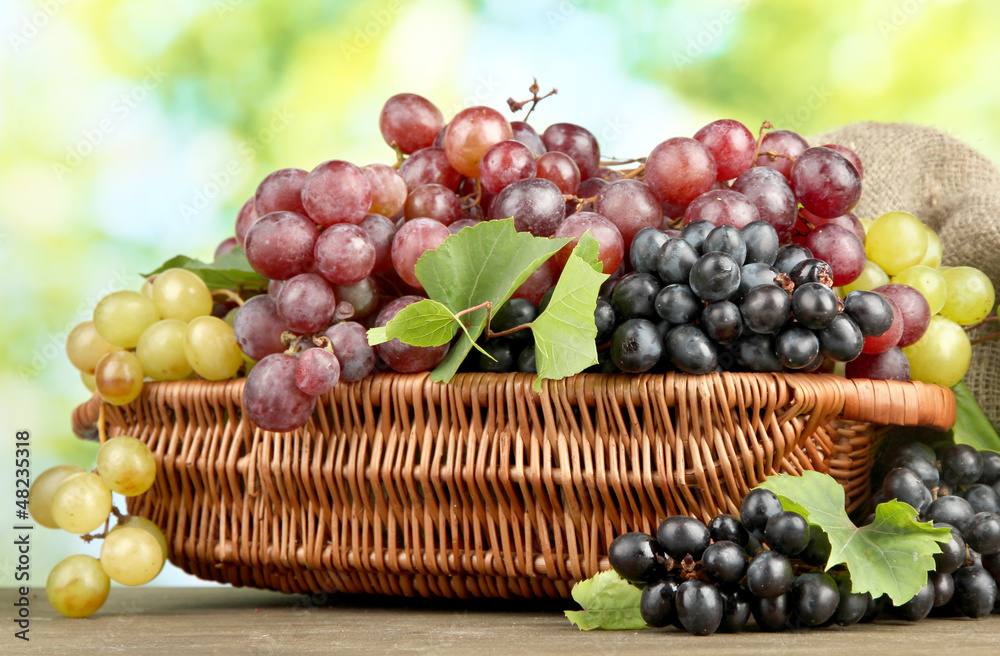 assortment of ripe sweet grapes in basket, on green background assortment of ripe sweet grapes in basket, on green background