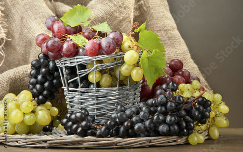 assortment of ripe sweet grapes in basket, on grey background