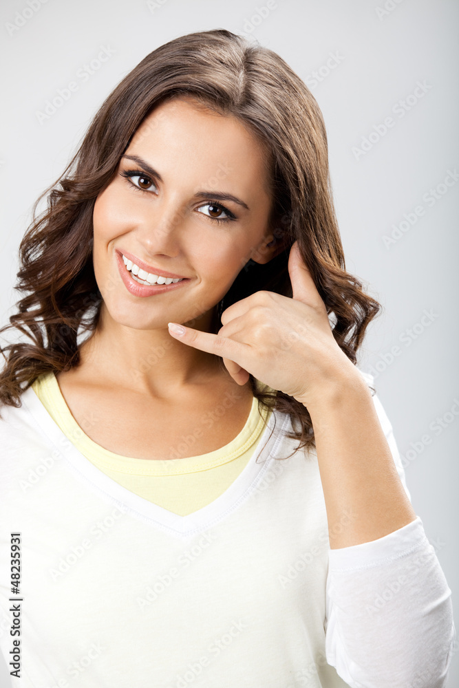 Young woman showing call me gesture, on gray