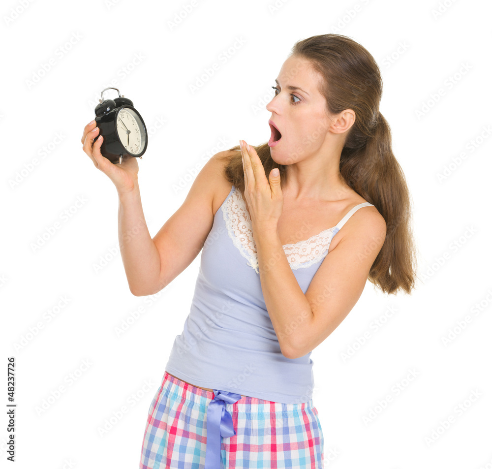 Fototapeta premium Shocked young woman in pajamas looking on alarm clock