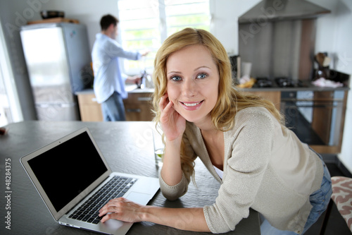 Cheerful blond girl connected on internet in home kitchen