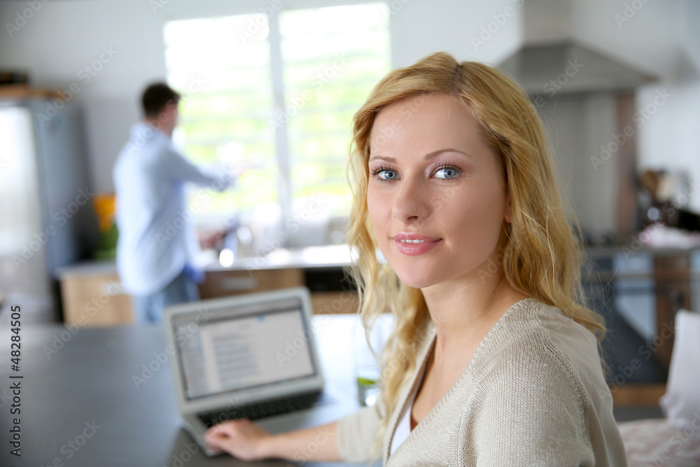 Cheerful blond girl connected on internet in home kitchen Cheerful blond girl connected on internet in home kitchen