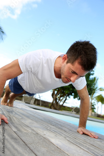Young man doing pushups on pool deck
