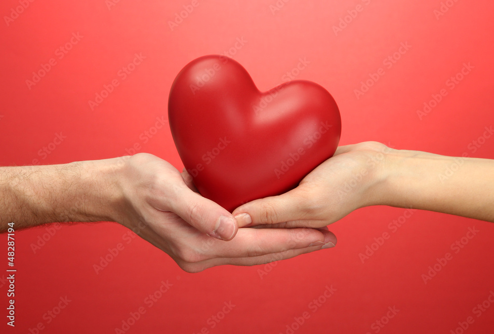 Obraz premium Red heart in woman and man hands, on red background