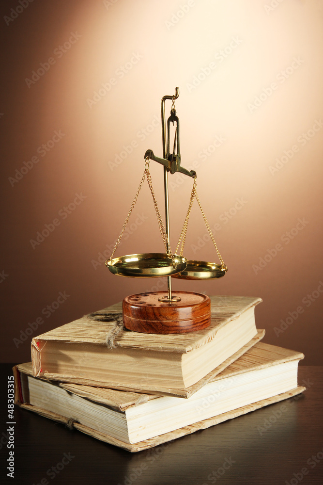 Gold scales of justice and books on brown background Gold scales of justice and books on brown background