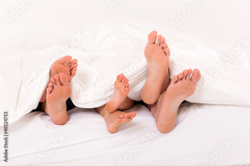 cute family lying under duvet on bed