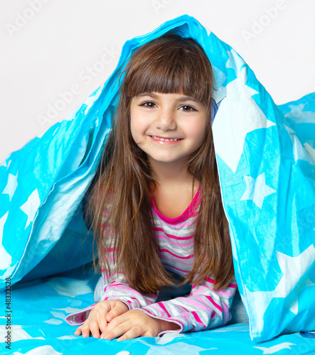beautiful little girl lying in bed under a blue blanket