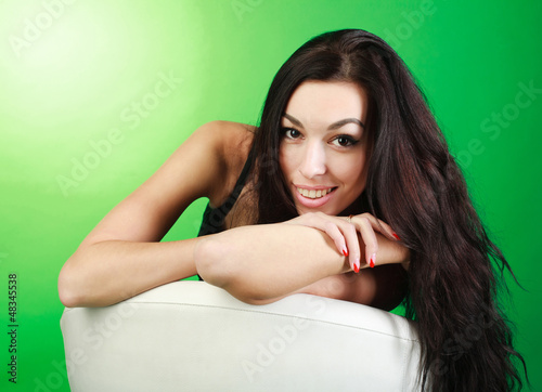 Young brunette girl sitting on white chair in studio  on green