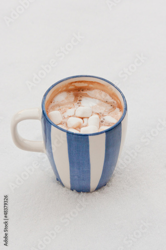 Cup of hot chocolate with melted marshmallows on snow