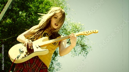 Young woman playing electric guitar outdoors. Old movie.