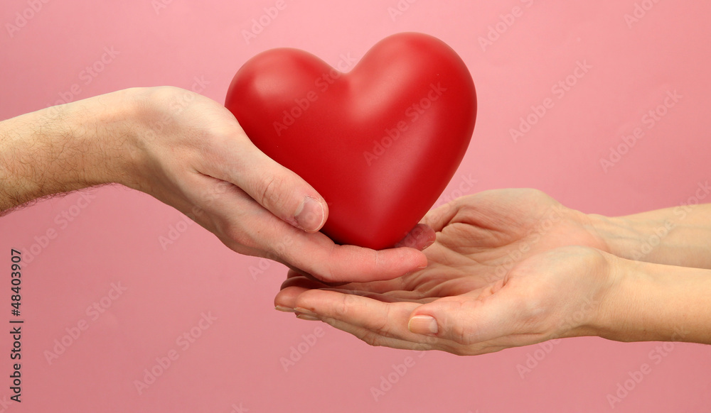 Obraz premium Red heart in woman and man hands, on pink background