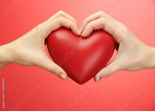Red heart in woman and man hands  on red background
