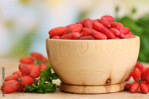 ripe barberries in wooden bowl with green leaves, on table