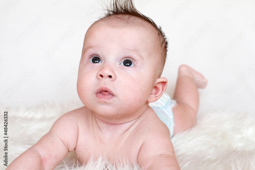 The surprised baby lies on a stomach on a fur plaid (3,5 months)