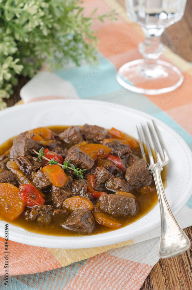 stew of beef with vegetables and prunes in a plate, vertical stew of beef with vegetables and prunes in a plate, vertical