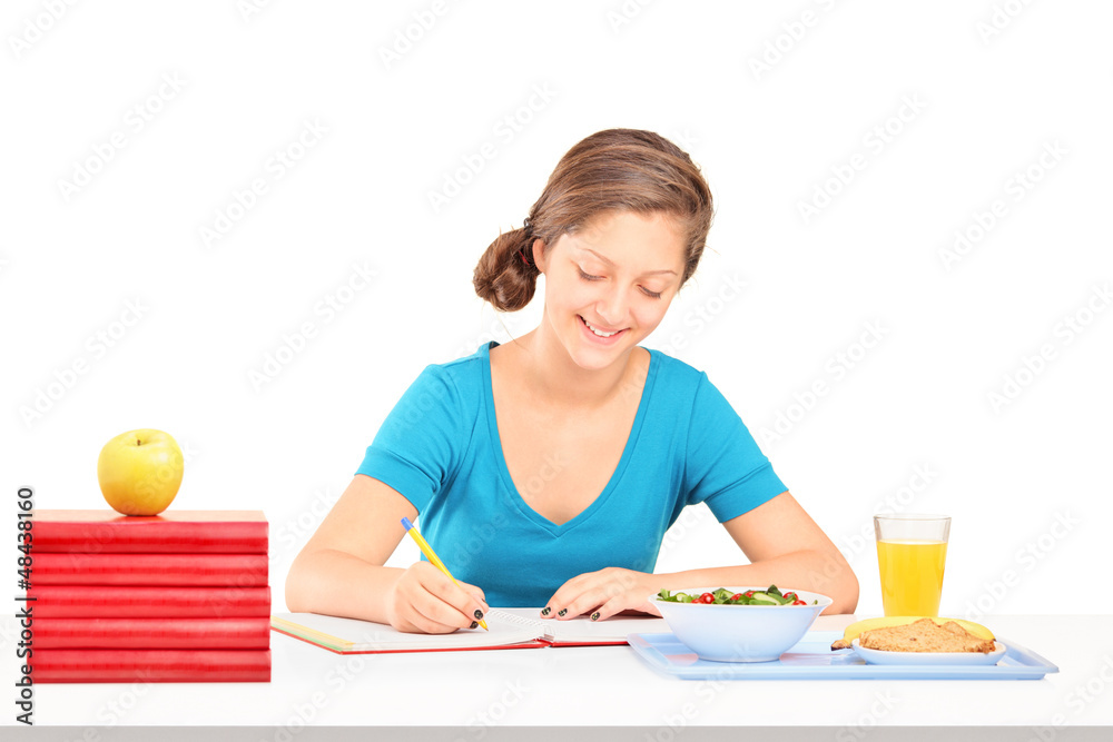 Teenage girl writing homework and having a meal