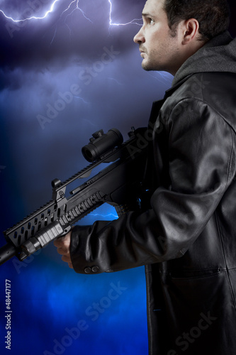 Man with long leather jacket and assault rifle over storm backgr