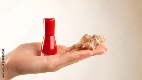Rotes Nagellackfläschchen mit Muschel auf Handfläche photo