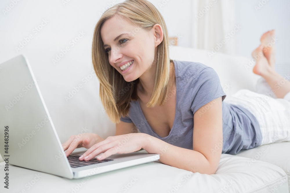 Casual woman lying on couch and using laptop Casual woman lying on couch and using laptop