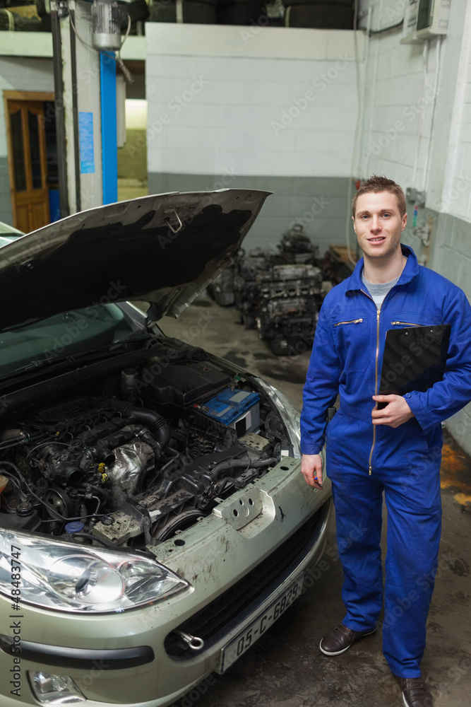 Confident mechanic standing by car with open hood Confident mechanic standing by car with open hood