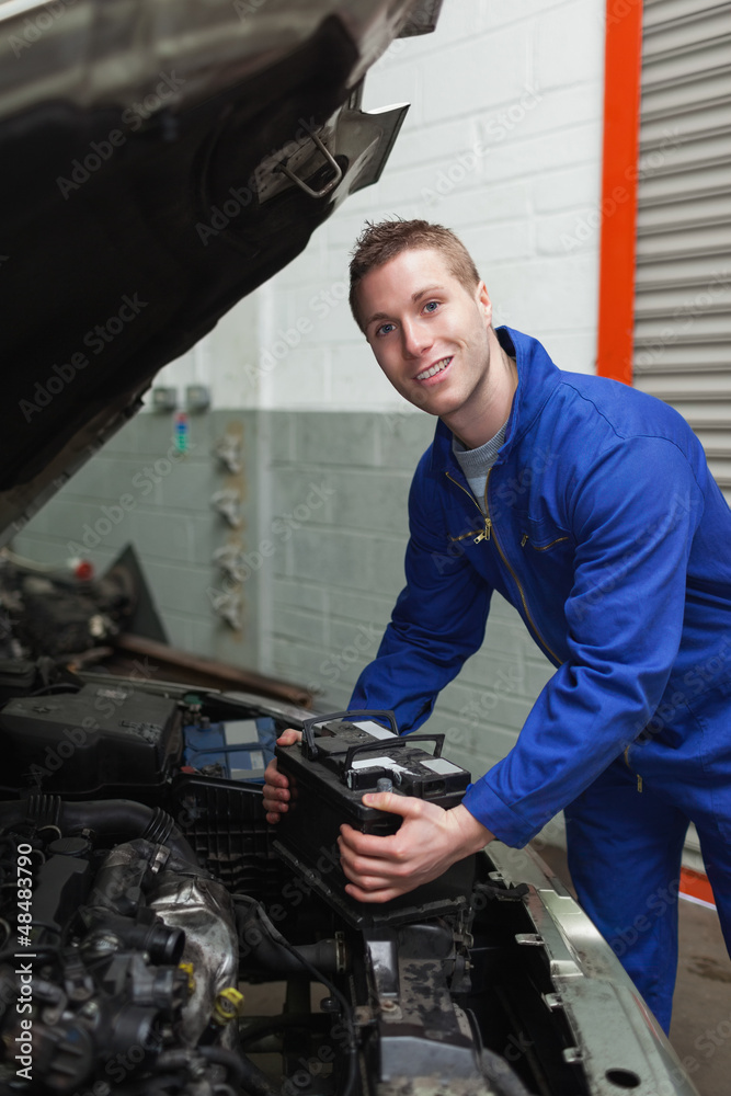 Happy mechanic with battery by car Happy mechanic with battery by car