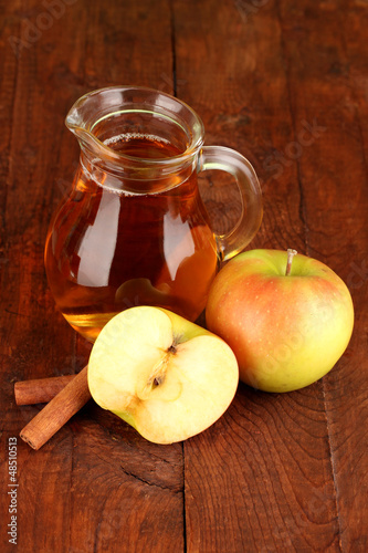 Full jug of apple juice and apple on wooden background