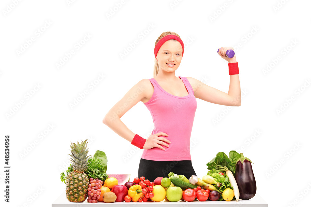 Young woman holding a dumbbell and posing with a pile of food Young woman holding a dumbbell and posing with a pile of food