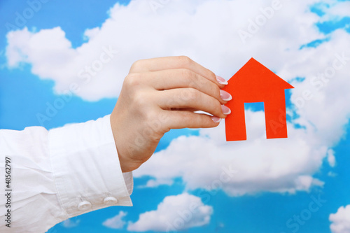 concept: woman hand with paper house on sky background, close