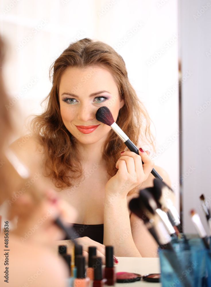 Young beautiful woman making make-up near mirror