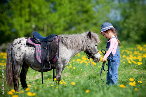 Child and small horse in the field at spring going to ride. photo