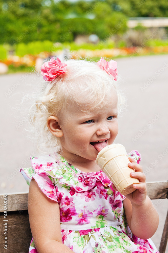The small blond girl eats ice-cream in a summer garden The small blond girl eats ice-cream in a summer garden