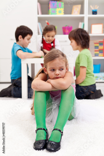 Sad little girl sitting excluded by the other kids