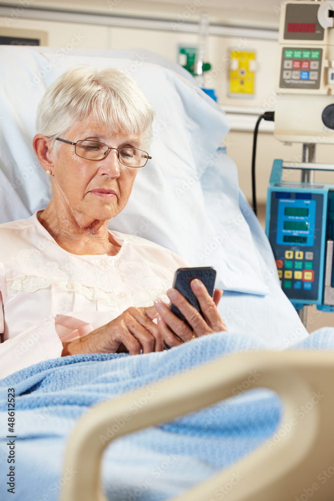 Obraz premium Senior Female Patient In Hospital Bed Using Mobile Phone
