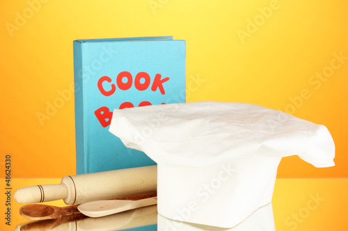 Fotografia Chef's hat with battledore and cook book on orange background