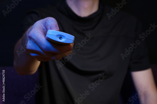 Man hand holding a TV remote control, on dark background