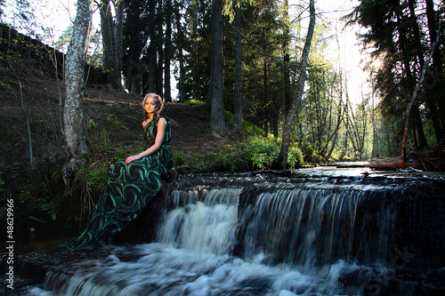 alone young nymph woman near waterfall in the forest