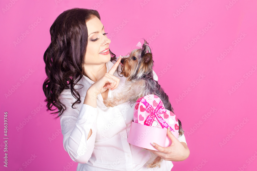 Young brunette with dog and gift box over pink background Young brunette with dog and gift box over pink background