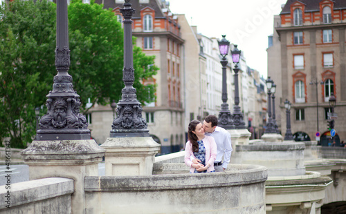 Dating couple is kissing tenderly in Paris on a bridge