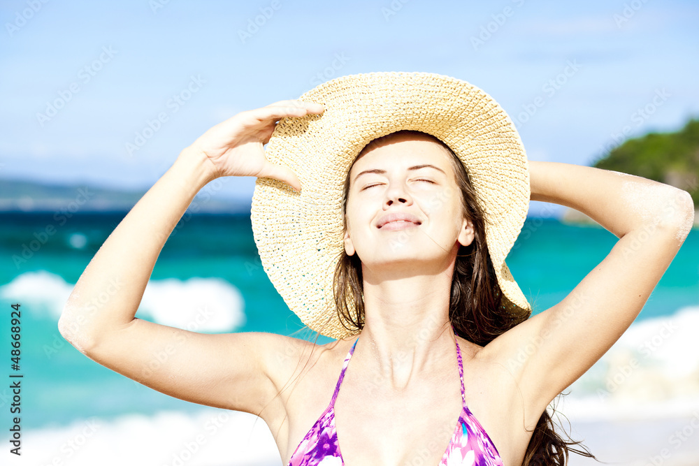 Happy woman smiling in straw hat with closed eyes on the beach