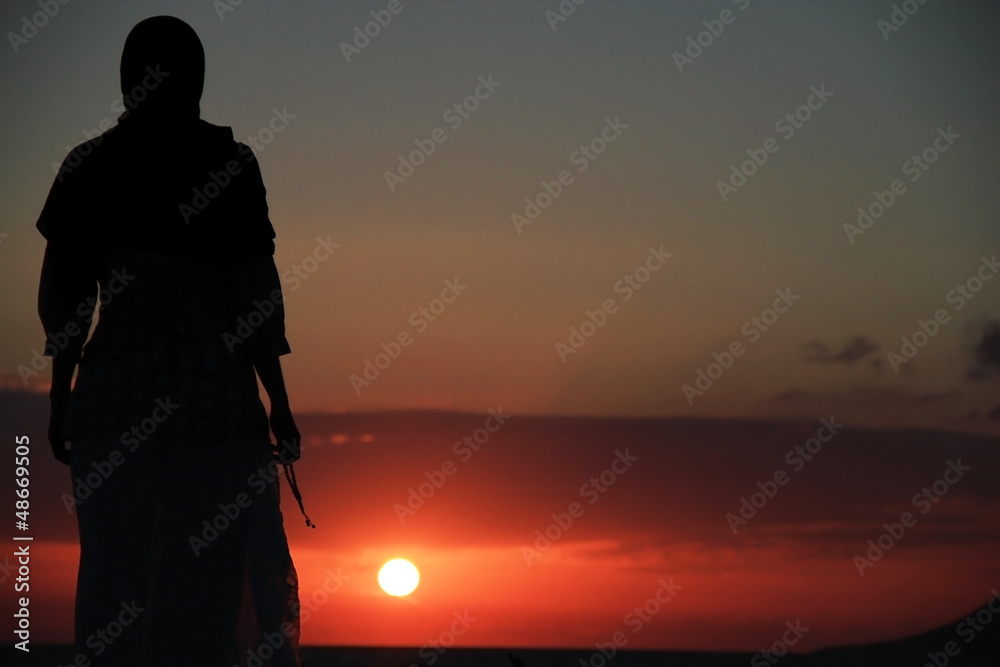 Obraz premium Young muslim woman praying at sunset