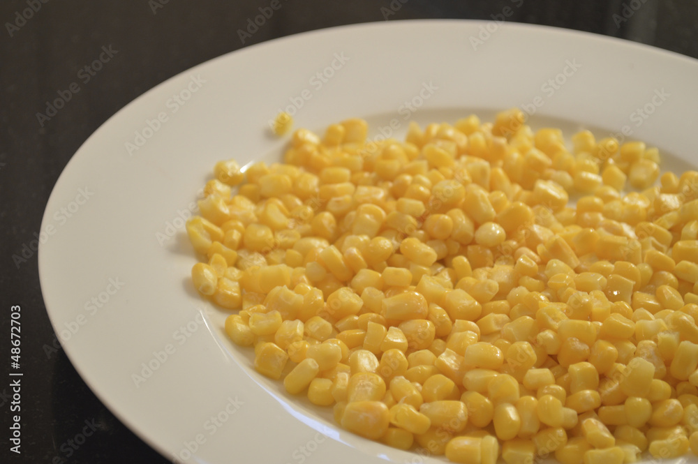 Yellow corn kernels on white plate with black background Yellow corn kernels on white plate with black background