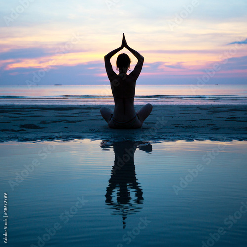 Silhouette of a woman yoga on sea sunset with reflection.