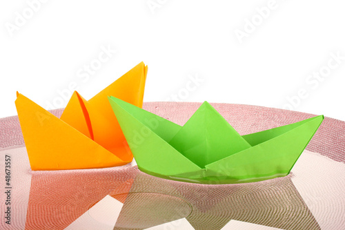 Color paper ship in water on pink plate, close-up