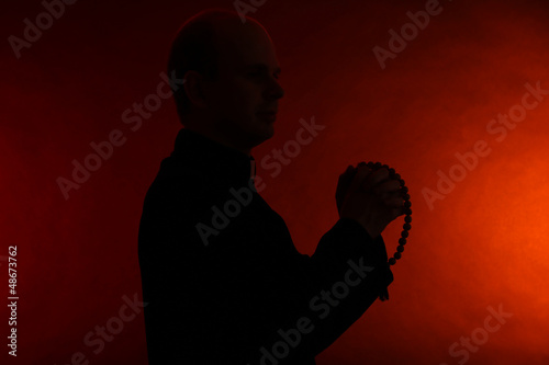 Billede på lærred Young pastor with wooden rosary, on dark red background
