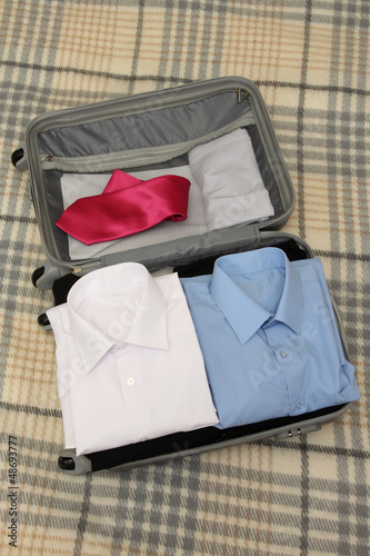 Open grey suitcase with clothing on plaid