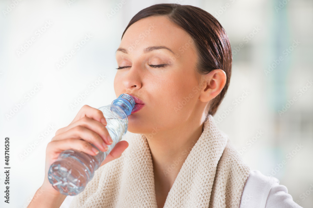 Portrait of young woman drinking water at gym after doing exerci Portrait of young woman drinking water at gym after doing exerci